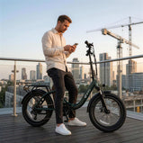 Zielony rower elektryczny DYU C9 na miejskim tarasie, obok którego stoi mężczyzna korzystający z telefonu, z panoramą miasta w tle.